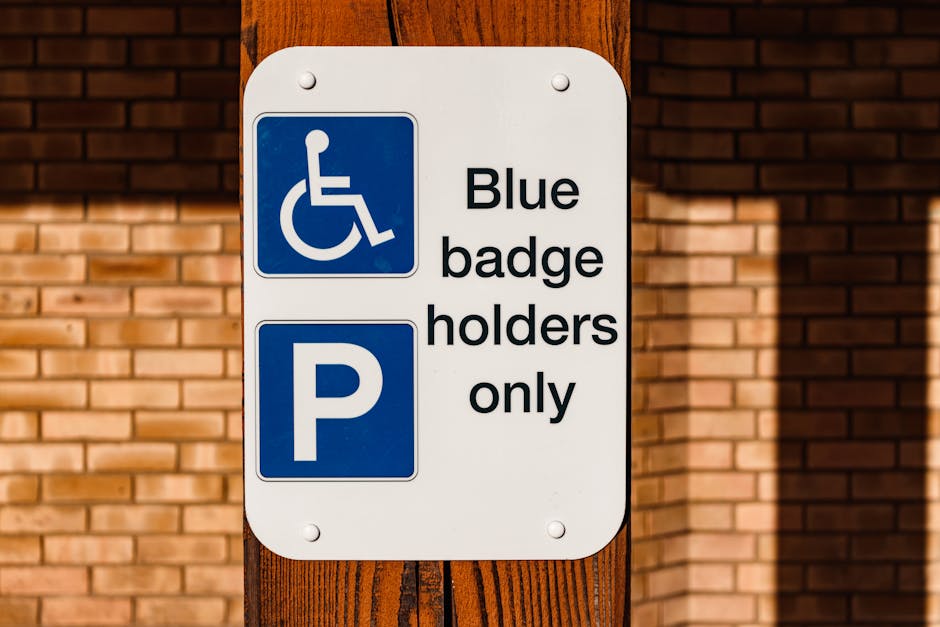 A rectangular white parking permit sign mounted on a wooden post in front of a brick wall. The sign features a blue wheelchair accessibility symbol at the top, indicating designated parking for disabled badge holders, followed by the text 'Blue badge holders only' in black. Below this, a large blue square with a white letter 'P' indicates parking. The sign is part of the signage used in parking areas for home relocation or moving services, such as those provided by Man with Van Totteridge, to ensure valid permit access during house removals in the Totteridge area. Lighting conditions suggest natural daylight, highlighting the textures of the brick wall and wooden post, with no visible vehicles or moving equipment in the scene.